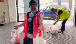 woman wearing a black beanie and pink high vis vest is carrying a bag of groceries in each hand